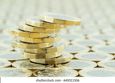 A precariously balanced stack of new one pound coins on a background of more money. The new British one pound coins were introduced in 2017