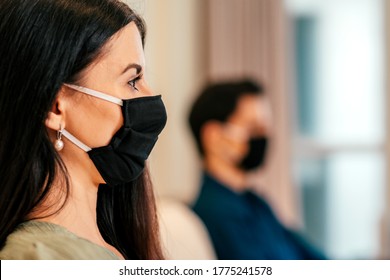 Precaution. Close Up Shot Of Young Dark-haired Woman Wearing Medical Mask, Sitting Indoors Together With Her Boyfriend. Relationship, Dating, Coronavirus, Covid 19 Concept. Side View