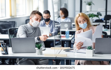 Precautions and social distancing in coronavirus pandemic. Millennial guy and girl in protective masks discussing and working with documents in workplace in office, panorama - Shutterstock ID 1819502675
