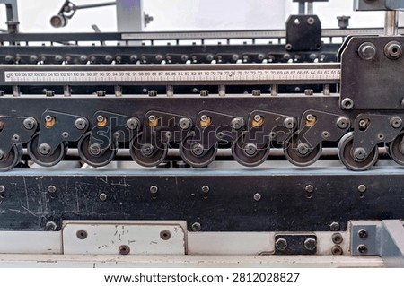 A precise alignment of industrial roller wheels on a automated conveyor system beneath a metal measurement ruler showing millimeter markings.
