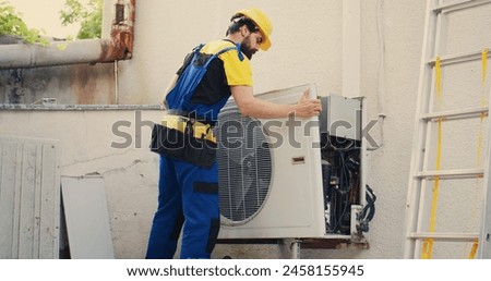 Precise serviceman starting work on malfunctioning outdoor air conditioner, dismantling condenser front coil panel. Proficient expert disassembling external hvac system to check for faulty wires