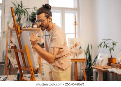 Precise skilled hipster painter standing at creative art studio with brush and palette in hands and creating unique artwork on easel. Portrait of tattooed artist standing at atelier and painting. - Powered by Shutterstock