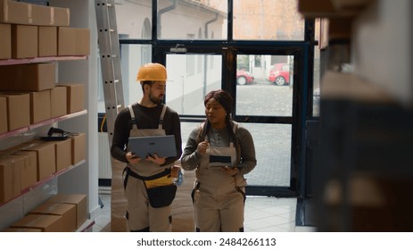 Precise workers preparing warehouse orders for delivery, using laptop and tablet to verify shipping informations, crosschecking online data with products labels in storage hub