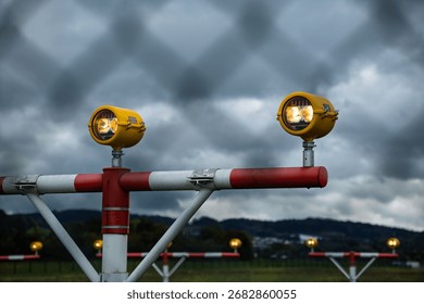 Precision Approach Path Indicator lights in front of an empty airport runway strip and edge lights. Close up shot of the light clusters, dark, moody, cloudy atmosphere, no people