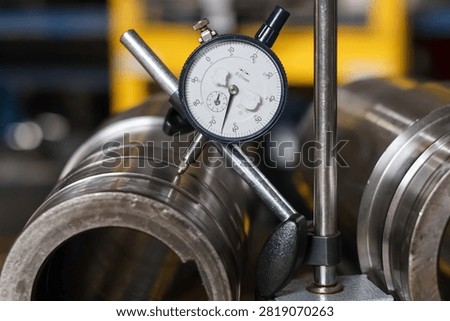 Precision dial indicator gauge measuring runout and tolerances on vehicle transmission metal shaft in workshop.