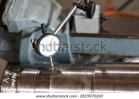 Precision dial indicator gauge measuring runout and surface accuracy on vehicle transmission shaft in workshop.