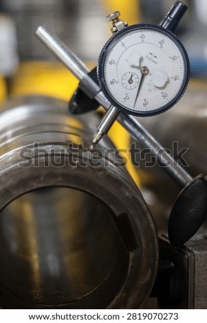 Precision dial indicator gauge measuring runout and tolerances on vehicle transmission metal shaft in workshop.