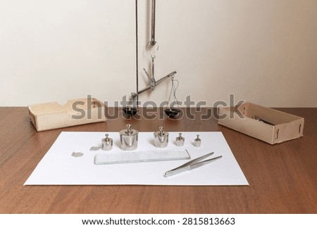 Precision laboratory measuring kit with calibration weights, balance scale, tweezers, glass plate and educational equipment on wooden table, physics and chemistry school experiment supplies