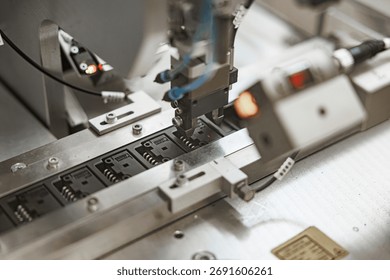 Precision robotic arm positioning electronic components onto black microchip carriers on an automated production line, with visible wiring and metallic guides