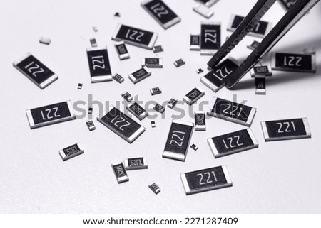 Precision tweezers picking tiny SMD resistors scattered on white background, electronic component assembly and quality control