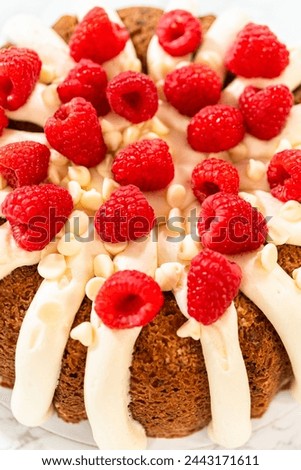 With precision, the White Chocolate Raspberry Bundt Cake is carefully removed from the pan - adorned with luscious cream cheese frosting, creating a delectable treat that is sure to delight.