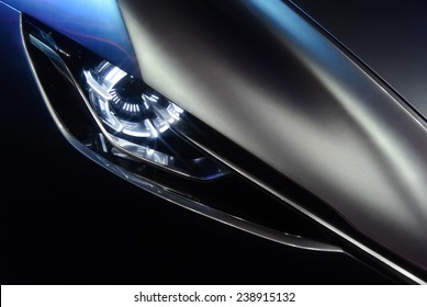 Predatory Car Headlight And Hood Of Powerful Sports Grey Car With Blue Glare On Dark Background