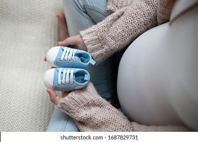 Pregnancy Anouncement Concept Detail Of Pregnant Mother To Be Belly Stomach Holding Blue Pair Of Tiny Baby Shoes 