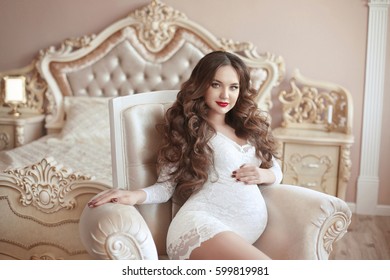 Pregnancy, Beautiful pregnant woman touching her belly with hands. Happy motherhood. Attractive brunette posing on modern armchair in luxury bedroom interior.  - Powered by Shutterstock