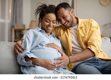 Pregnancy. Black Husband And Pregnant Wife Hugging Sitting At Home. Family Couple Expecting Baby, Man Embracing Woman Smiling Posing Together. Childbirth Concept