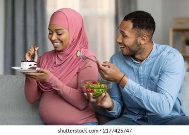 Pregnancy Cravings. Black Man Offering Salad To His Pregnant Muslim Wife While She Eating Cake, Islamic Lady In Hijab Choosing Sweets Over Vegetables While Awaiting Baby, Refusing Healthy Nutrition