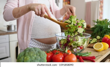 Pregnancy Diet Nutrition Concept. Pregnant Woman Preparing Meal On Kitchen, Making Salad. - Shutterstock ID 1591858090