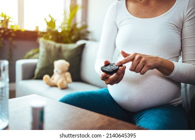 Pregnancy, health and glycemia concept - pregnant beautiful woman checking blood sugar level with glucometer and lancing device at home