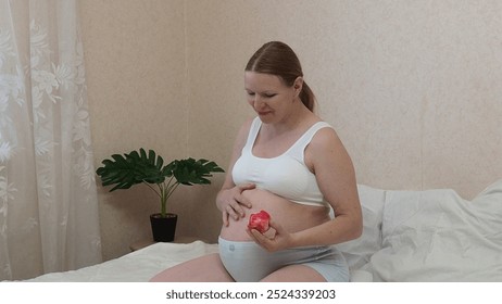 pregnancy, healthy food and people concept - happy pregnant woman eating apple at home. Beautiful pregnant woman smiling sitting on a couch. The happiest time for every woman. Fruit in the hands. - Powered by Shutterstock