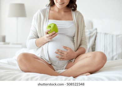 pregnancy, healthy food and people concept - close up of happy pregnant woman eating green apple at home - Powered by Shutterstock