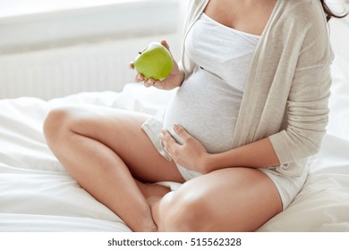 Pregnancy, Healthy Food And People Concept - Close Up Of Happy Pregnant Woman Eating Green Apple At Home