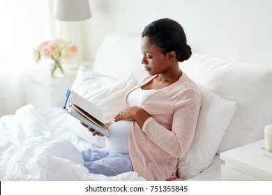 pregnancy and leisure concept - smiling pregnant african american woman reading book in bed at home