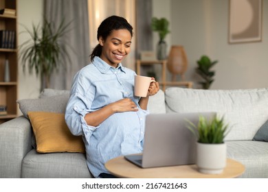 Pregnancy Lifestyle. Happy Pregnant African American Woman Using Laptop Computer Watching Movie Online And Drinking Coffee Sitting On Couch At Home. Internet Technology Concept - Powered by Shutterstock