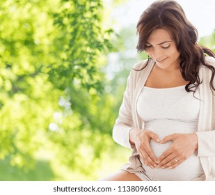 pregnancy, love, people and expectation concept - happy pregnant woman making heart gesture over green natural background