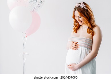 Pregnancy Model Shooting. Happy Woman. Expecting New Life. Motherhood Beauty. Smiling Tummy Lady Touching Baby Bump Isolated White Pastel Balloons Decoration Copy Space.