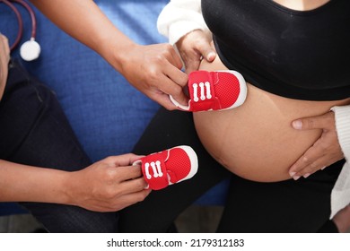 Pregnancy Mother And Father Hold Red Shoes On Mom's Tummy .   Woman Has Baby In Her Stomach Waiting For Baby Will Be Born Soonest. Dad's Hands  On Tummy Together.