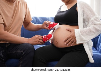 Pregnancy Mother And Father Hold Red Shoes On Mom's Tummy .   Woman Has Baby In Her Stomach Waiting For Baby Will Be Born Soonest. Dad's Hands  On Tummy Together.