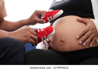 Pregnancy Mother And Father Hold Red Shoes On Mom's Tummy .   Woman Has Baby In Her Stomach Waiting For Baby Will Be Born Soonest. Dad's Hands  On Tummy Together.