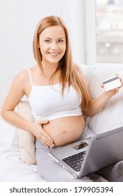 Schwangerschaft, Mutterschaft, Geld, Internet- und Technologiekonzept - Lächelnde schwangere Frau auf einem Sofa mit Laptop und Kreditkarte