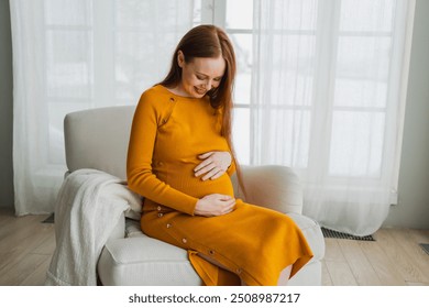 Pregnancy motherhood people expectation future. Pregnant woman with big belly sitting on chair near window at home. Girl hugging her tummy enjoying pregnancy. Maternity tenderness parenthood new life - Powered by Shutterstock