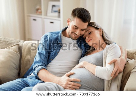 pregnancy and people concept - happy man hugging pregnant woman at home