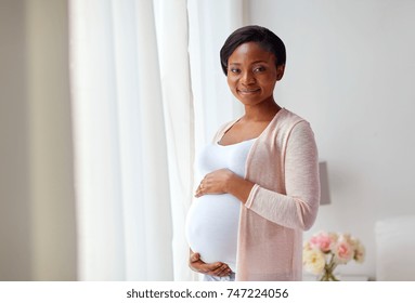 pregnancy, people and expectation concept - happy pregnant african american woman at home window