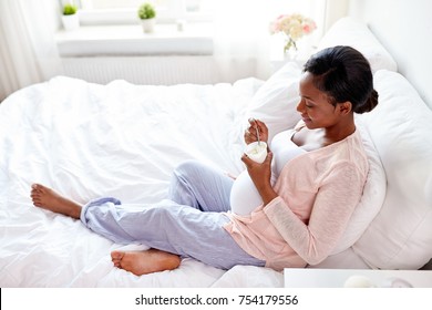 pregnancy, people and food concept - happy pregnant african american woman eating yogurt in bed at home