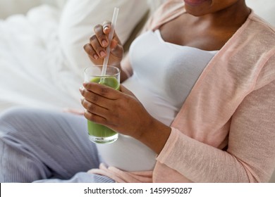 Pregnancy, People And Rest Concept - Close Up Of Happy Pregnant African American Woman Drinking Green Smoothie In Bed At Home