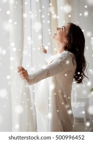 Pregnancy, People, Winter, Christmas And Expectation Concept - Happy Pregnant Woman Opening Window Curtains At Home Over Snow