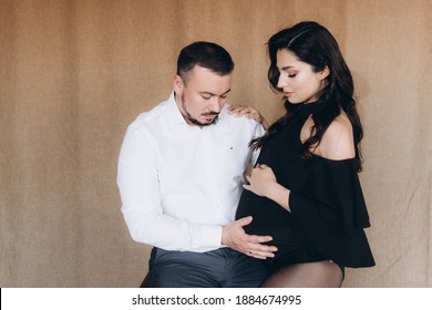 Pregnancy Photo Session In A Photo Studio With A Fabric Background In A Black Bodysuit And Tights