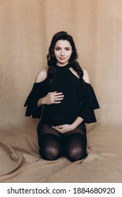 Pregnancy Photo Session In A Photo Studio With A Fabric Background In A Black Bodysuit And Tights