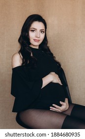 Pregnancy Photo Session In A Photo Studio With A Fabric Background In A Black Bodysuit And Tights