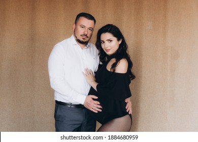 Pregnancy Photo Session In A Photo Studio With A Fabric Background In A Black Bodysuit And Tights