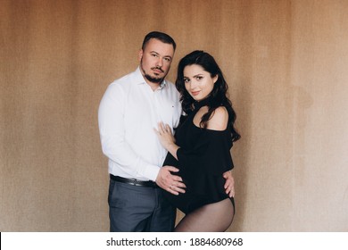 Pregnancy Photo Session In A Photo Studio With A Fabric Background In A Black Bodysuit And Tights