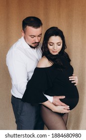 Pregnancy Photo Session In A Photo Studio With A Fabric Background In A Black Bodysuit And Tights