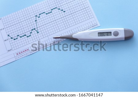 Pregnancy planning. Measurement of basal body temperature. Thermometer, temperature graph on a blue background. Copy space