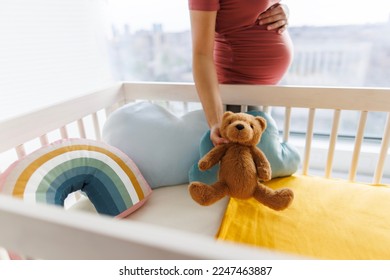 Pregnancy. Pregnant woman preparing nursery holding belly baby bump by crib holding teddy bear. regnancy concept and home nusery planning - Powered by Shutterstock