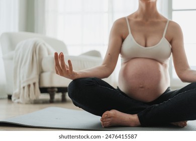 Pregnancy prenatal breathing. Pregnant woman with big belly sitting in lotus pose on yoga matt at home. Pregnant girl practicing yoga mindfulness meditation. Relaxation self care during pregnancy - Powered by Shutterstock