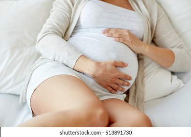pregnancy, rest, people and expectation concept - close up of pregnant woman lying in bed and touching her belly at home