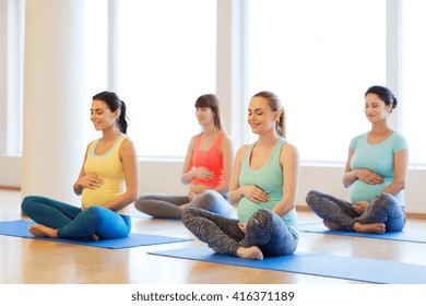 Pregnancy, Sport, Fitness, People And Healthy Lifestyle Concept - Group Of Happy Pregnant Women Exercising Yoga And And Meditating In Lotus Pose In Gym